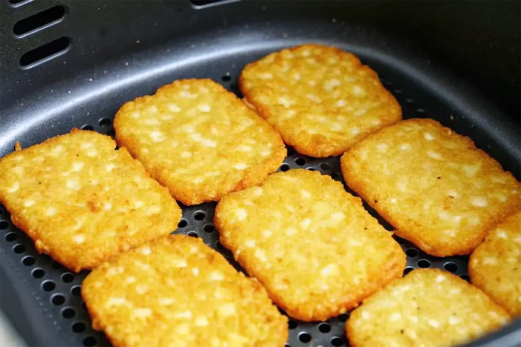 Hash browns arranged in a single layer inside an air fryer basket, golden brown and ready to eat.