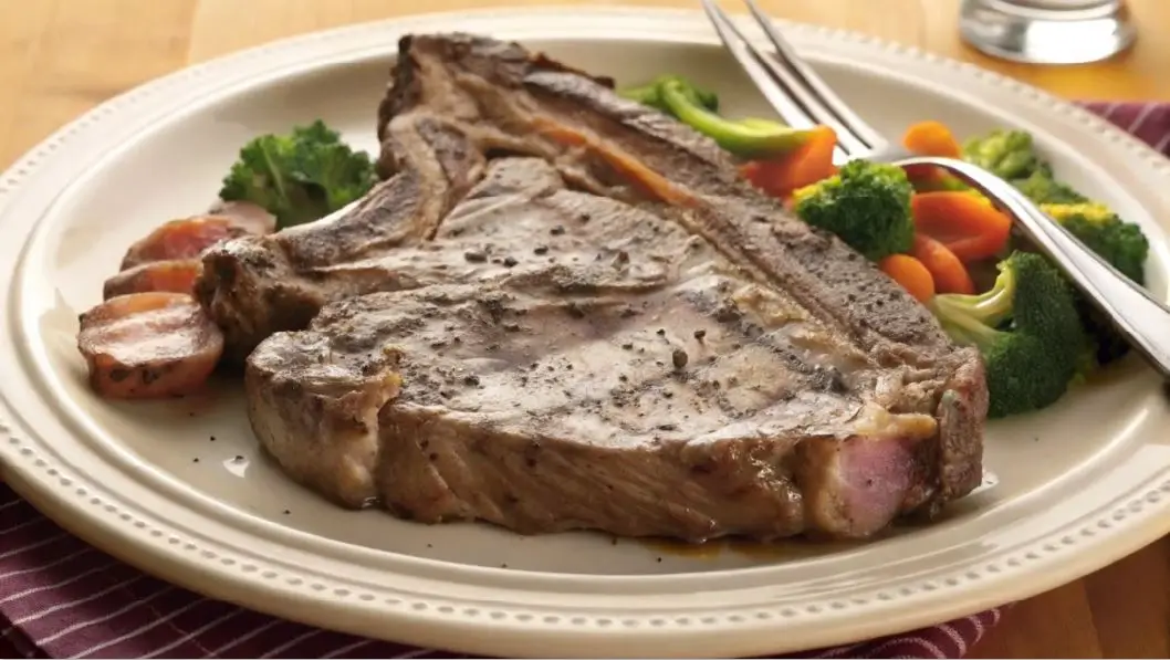 A grilled chuck eye steak served on a plate with roasted vegetables, including potatoes and carrots, garnished with fresh parsley.