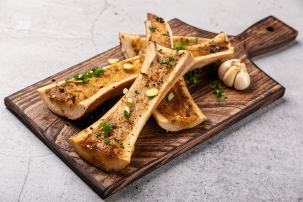 What is a Soup Bone Slang? Grilled bone marrow served on a wooden cutting board, garnished with fresh herbs and garlic.