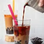 Homemade boba tea with black tapioca pearls, milk tea, and ice in a clear glass
