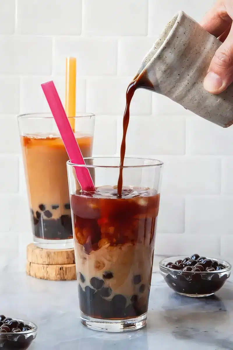 Homemade boba tea with black tapioca pearls, milk tea, and ice in a clear glass
