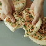 Garlic and butter flatbread being pulled apart to show soft, fluffy interior with herbs