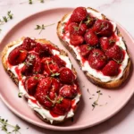 Roasted strawberry whipped ricotta toast on pink plate with fresh thyme: jammy honey-roasted berries over creamy ricotta on crispy sourdough bread.